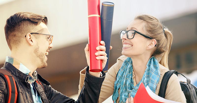 Man and woman holding their degrees