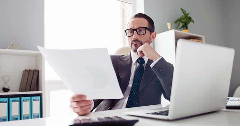 Business man examining a document while sitting at his desk